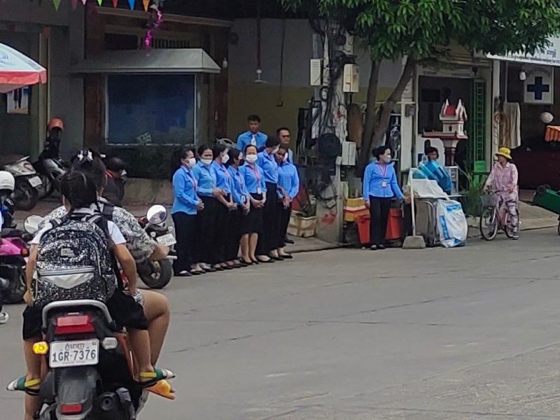 Учителя в униформе стоят в шеренге у школы в Пномпене